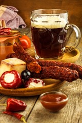 Dark beer in a glass and spicy sausages with chili peppers. Dried sausages on the table.