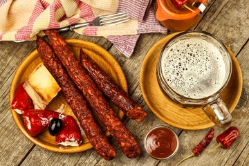 Dark beer in a glass and spicy sausages with chili peppers. Dried sausages on the table.