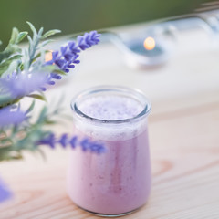 Glass of yogurt with blueberries. Homemade yogurt with blueberry in jars in an orchard in summertime. Evening light. Bouquet of flowers. Blurry background. Soft focus. Closeup. Macro.