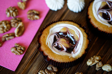 Fototapeta premium Round cake with fruit jam and creamy filling on a wooden background. Nearby are a pink napkin, walnuts and meringues. Dessert and sweets