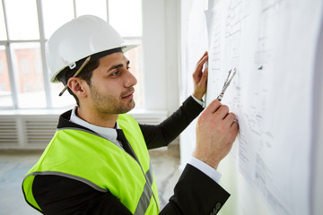 Side view portrait of  Middle-Eastern engineer  holding plans against wall  while standing on...