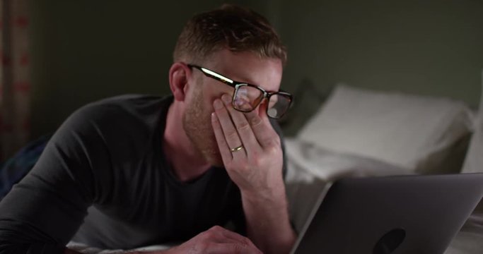 4K Exhausted man working late on computer and rubbing his eyes with tiredness