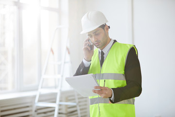 Waist up portrait of project manager wearing hardhat speaking by phone while standing on construction site, copy space