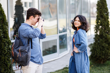 Fototapeta premium Young cute couple - a boy and a girl walking around the city and photographed. A couple have fun spending time together. Date two nice people in the park