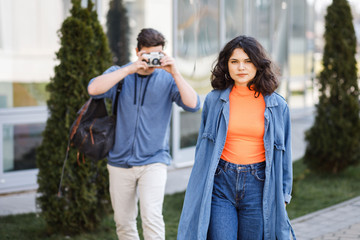 Fototapeta premium Young cute couple - a boy and a girl walking around the city and photographed. A couple have fun spending time together. Date two nice people in the park