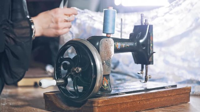 Old black sewing machine on the background of a female tailor at work in atelier. Professional seamstress working in the workshop with beautiful material.