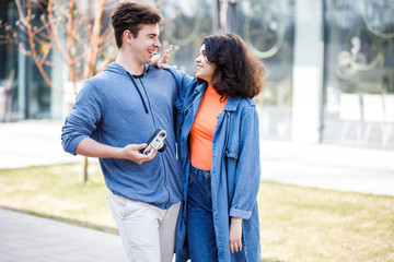 Obraz premium Young cute couple - a boy and a girl walking around the city and photographed. A couple have fun spending time together. Date two nice people in the park
