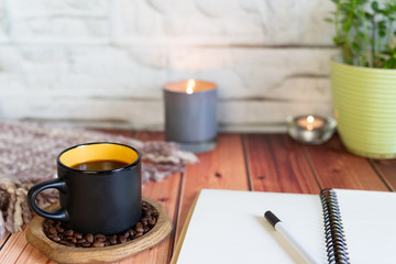 A Cup of coffee on a wooden table with a potted plant and candle