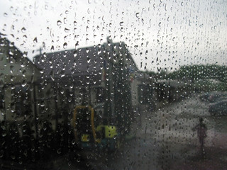 Walk in the rain of person near roadside cafe. View through wet glass with raindrops. Blurred background. Selective focus.