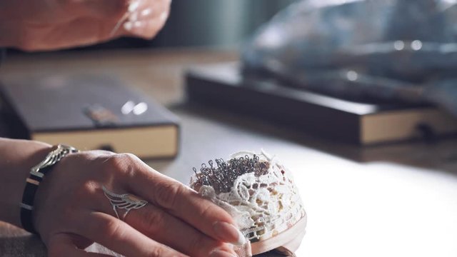 Young tailor is taking spoos from the beautiful pincushion. Many black sewing pins in a small white pillow for seamstress on the wooden table.