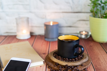 A Cup of coffee on a wooden table with a candle and smartphone