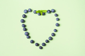 Fresh blueberries in shape of heart frame on pastel green background. Healthy breakfast concept