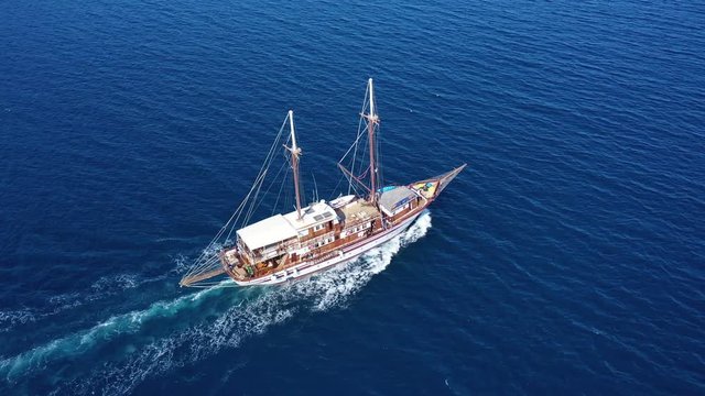 Aerial birds eye drone view video of beautiful wooden sailboat cruising in deep blue sea of Mykonos island, Cyclades, Greece