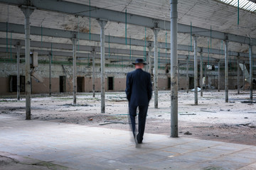 Mann im Anzug und Hut läuft durch eine verlassene Industrieanlage
