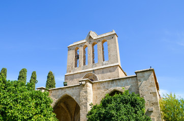 Fototapeta na wymiar Historical building in Cypriot Bellapais Abbey complex in city Bellapais, Turkish Northern Cyprus taken from below with blue sky above and green trees around. Popular tourist spot