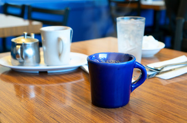 Blue steaming mug of black coffee on a table in a cafe
