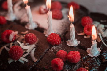 tasty homemade chocolate birthday cake decorated of some raspberries and candles served on the gentle pink background