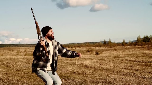 Man holding shotgun. Mountain hunting. Hunter is on a forest clearing and cocks his shotgun in booty.