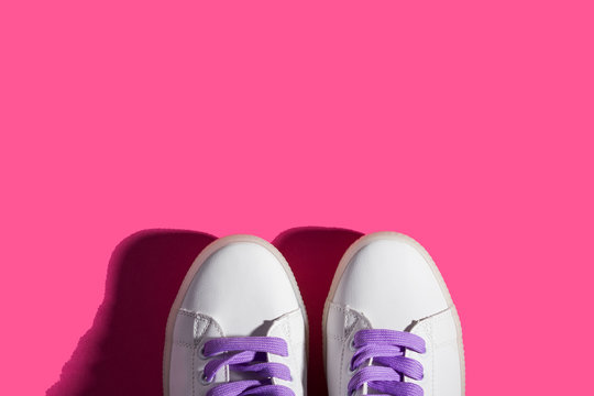 White sneakers with purple laces on pink background. Shadow. Modern minimal fashion art trendy bold color flat lay backdrop