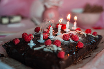 tasty homemade chocolate birthday cake decorated of some raspberries and candles served on the gentle pink background