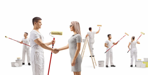 Obraz premium Male painter shaking hands with a young woman and workers painting wall
