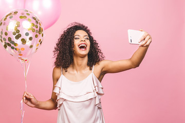 Self portrait of afro american positive girl in dress having balloons in hand shooting selfie on...