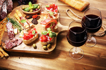 Traditional italian antipasto bruschetta appetizer with cherry tomatoes, cream cheese, basil leaves and balsamic vinegar on cutting board with prosciutto, salami, cheese