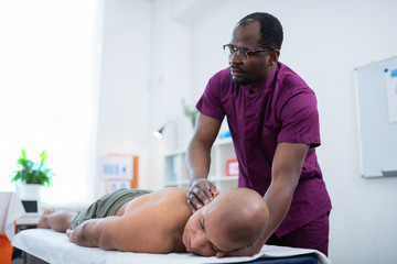 Obraz premium Dark-skinned massage therapist in glasses working with sportsman