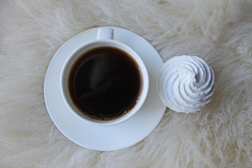 Black coffee in white Cup on saucer with meringue cube puzzle laptop on fluffy beige skin