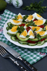 Healthy salad of avocado, cucumbers, eggs and sweet pepper located in a plate on a dark background
