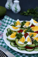 Healthy salad of avocado, cucumbers, eggs and sweet pepper located in a plate on a dark background