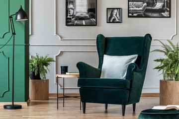 Pillow on emerald green armchair in elegant living room with black and white photos on grey wall