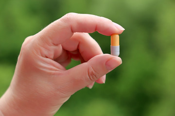 Medication in capsule in female hand on blurred green nature background. Concept of vitamins for beauty, diet pill, health care, natural drug