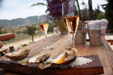 Pair of glasses one with sparkling pink wine and another with red wine placed on wooden table for pairing with oysters cooked in gourmet style