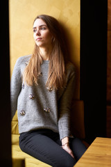 Portrait young pretty pensive girl with long hair and natural make-up in the cafe.