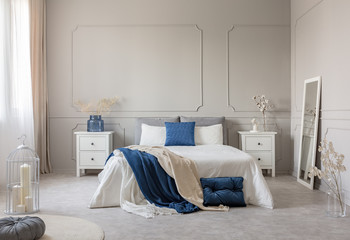 Blue pillow and blanket on white bed in spacious bedroom interior, copy space on empty grey wall