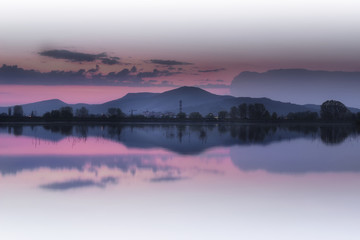 Distant mountain and cityscape reflection in a calm lake during blue hour with dramatic, purple sky and clouds