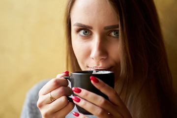 Attractive girl with long hair and lips in the foam holding cup of cappuccino and drinking coffee...