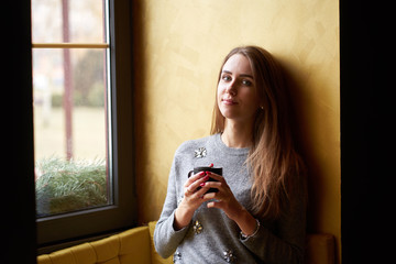Young pretty girl with long hair drinking coffee or tea  in the cafe.