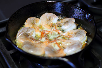 Shrimp cooking in butter and garlic in a cast iron skillet on the  stove.