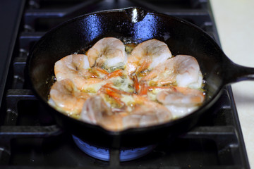 Shrimp cooking in butter and garlic in a cast iron skillet on the  stove.