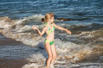 beautiful and happy girl in a green swimsuit throws a pebble in the sea, beach concept