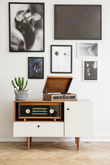 White wooden dresser with vintage radio and old gramophone. Gallery of prints on the wall. Real photo concept
