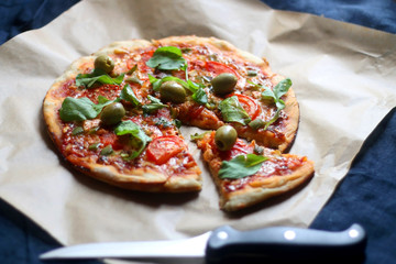 Homemade vegetarian pizza with tomato sauce, two types of cheese, tomatoes, peppers, arugula, olives and herbs. Selective focus.