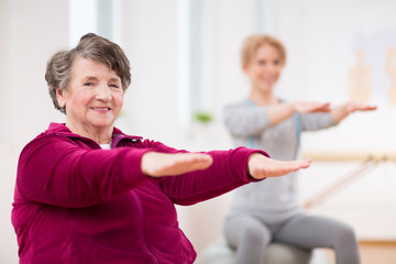 Smiling elderly lady holding her arms during pilates for seniors