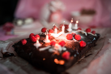 tasty homemade chocolate birthday cake decorated of some raspberries and candles served on the gentle pink background
