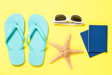 Blue flip flops, sunglasses, passport and starfish on yellow.
