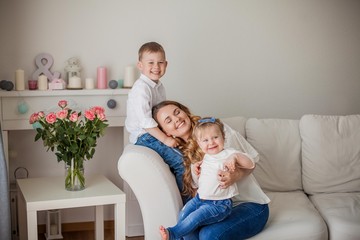 Beautiful young mother, little son, little daughter are sitting on the sofa at home. Mothers Day. A happy family. Cozy.