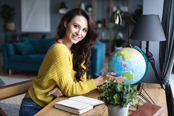 Beautiful smiling woman at the table with a model of the globe, choosing a country to travel.