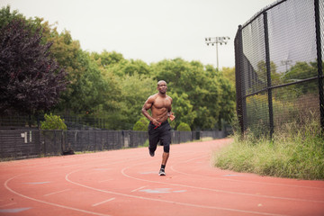 Fototapeta premium Full length of shirtless male athlete running on sports track against trees